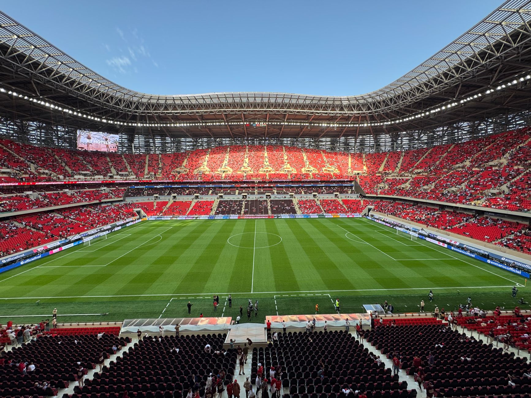 A vibrant football stadium with a broad green field and red seats filled with sports fans.