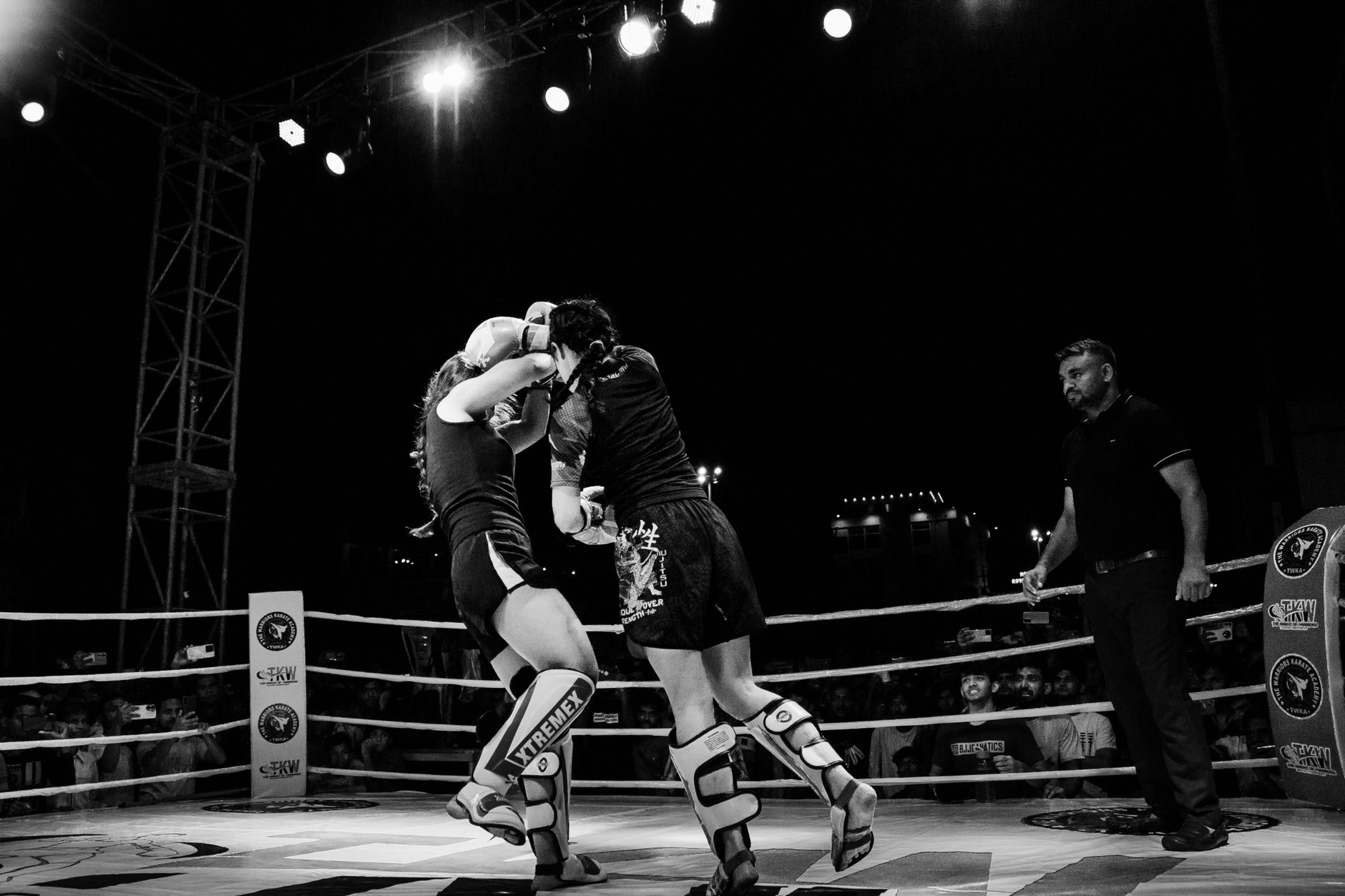 Two female fighters in an intense boxing match captured in dramatic black and white photography.