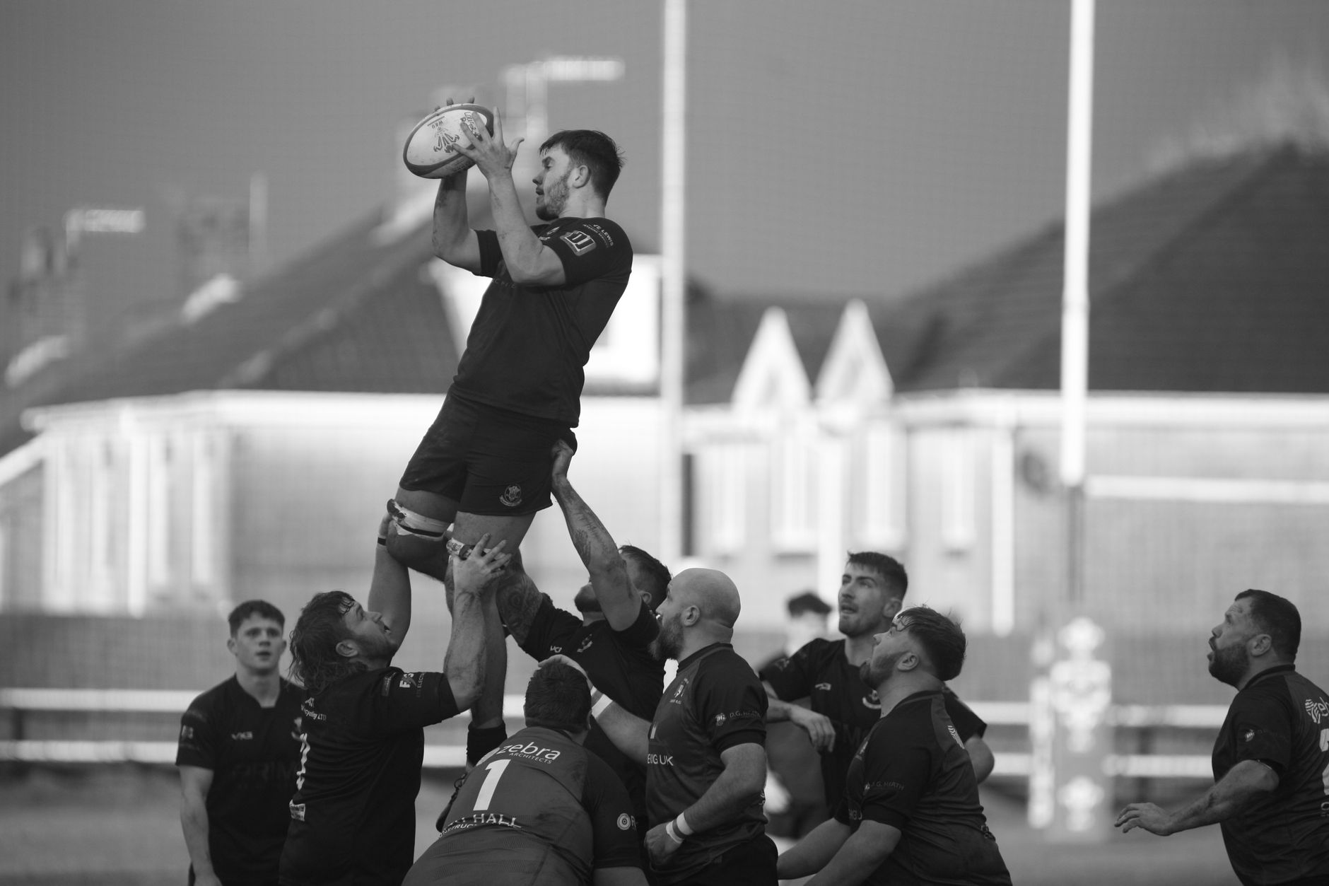 A dynamic black and white photo capturing a rugby player lifted during a competitive match.