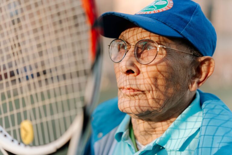 A senior man in sportswear standing with a tennis racket outdoors, enjoying leisure time.