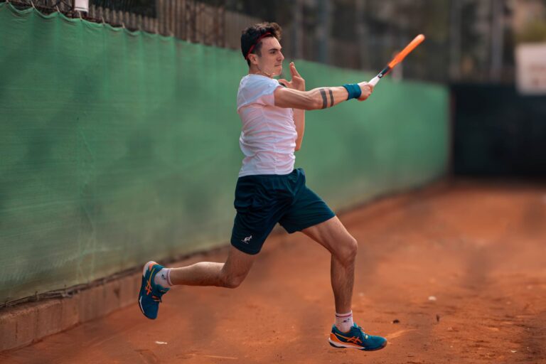 A focused tennis player mid-swing on a clay court, showcasing energy and sportsmanship.