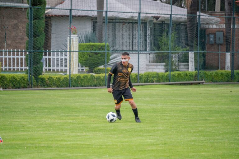 A young soccer player in black sportswear dribbling a ball on a green field in Texcoco, Mexico.