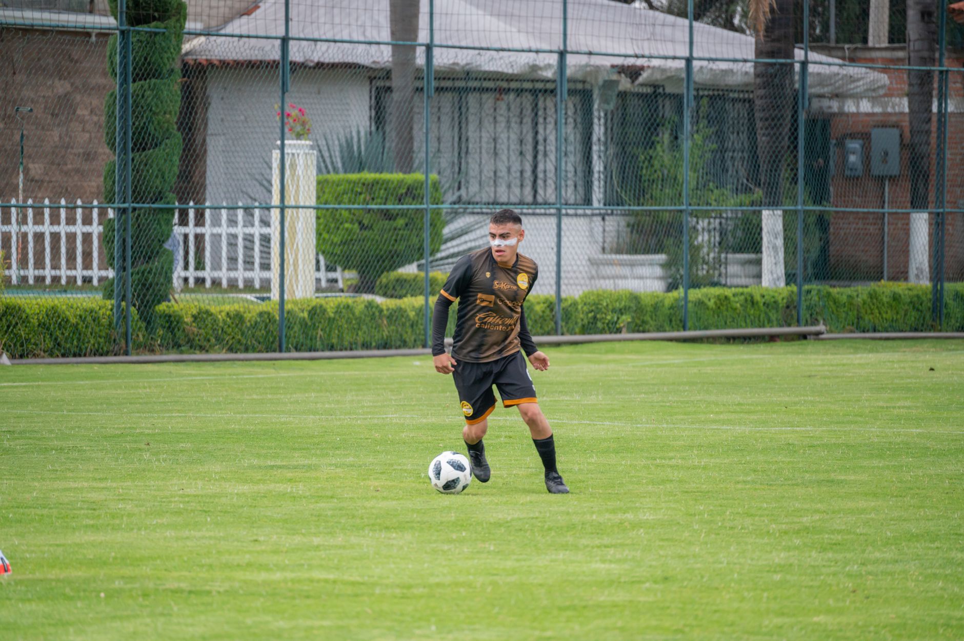 A young soccer player in black sportswear dribbling a ball on a green field in Texcoco, Mexico.