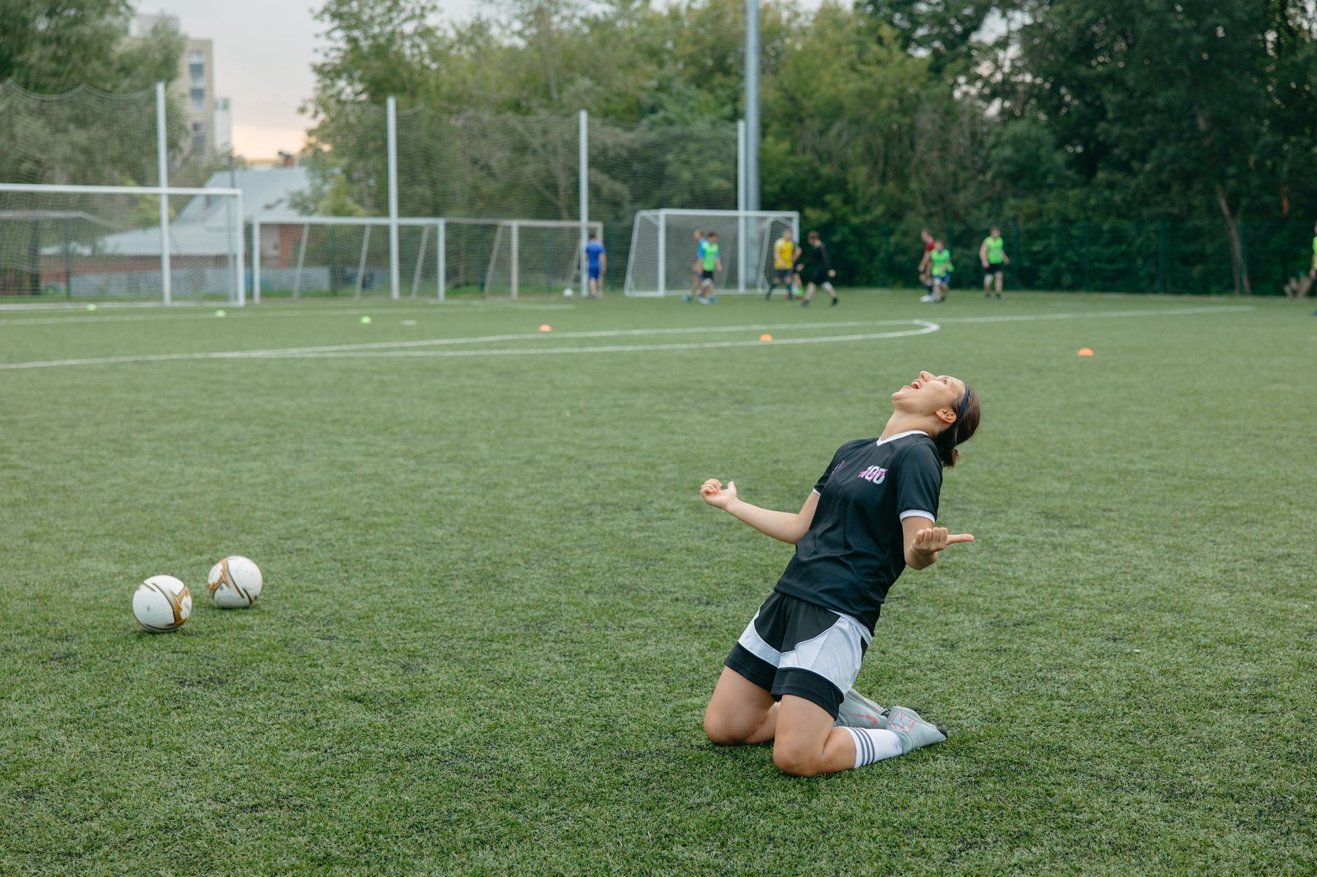 Female soccer player celebrating with arms raised on outdoor field.