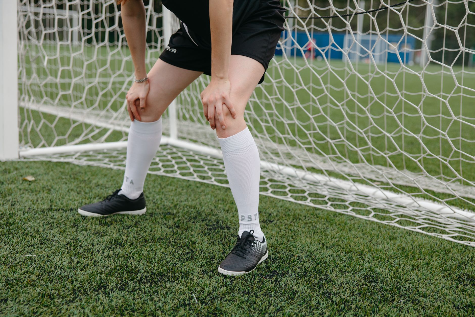 Soccer player resting in front of the goal on a grassy field, wearing sports uniform and sneakers.