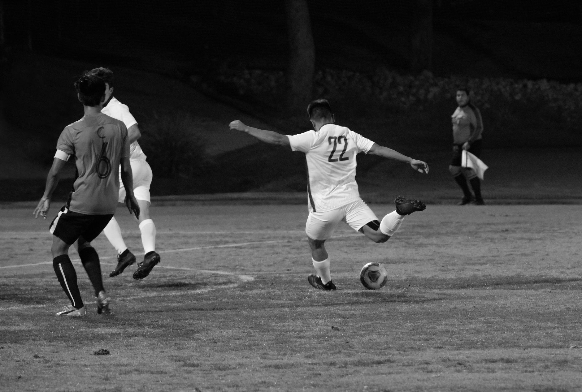 Black and white full body of male football player kicking ball during play in field