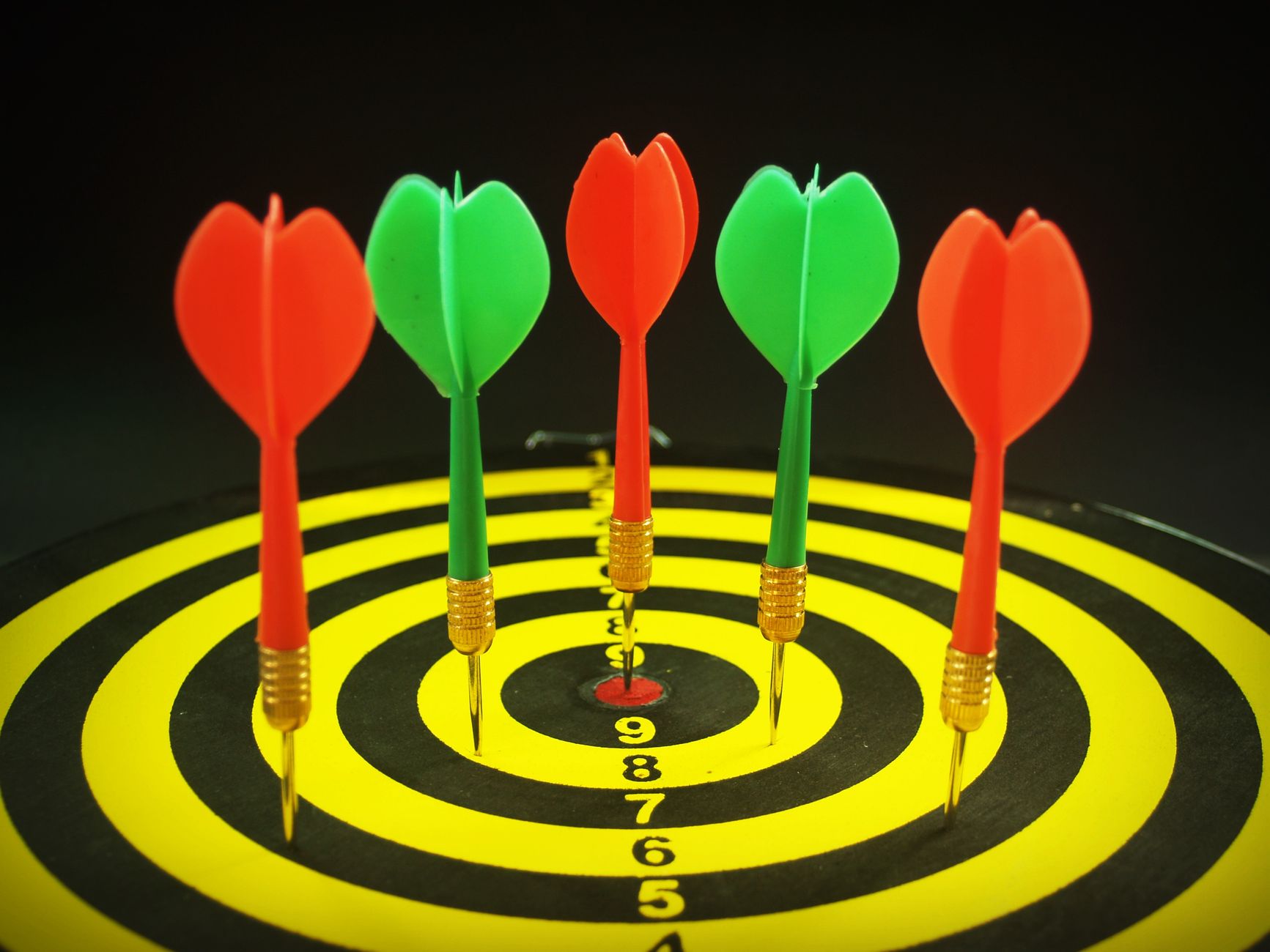 Close-up of colorful darts hitting the bullseye on a dartboard, showcasing precision and focus.