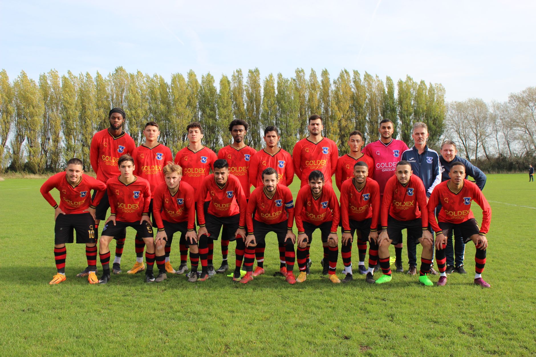 A local soccer team posing on a sunny day on the field.