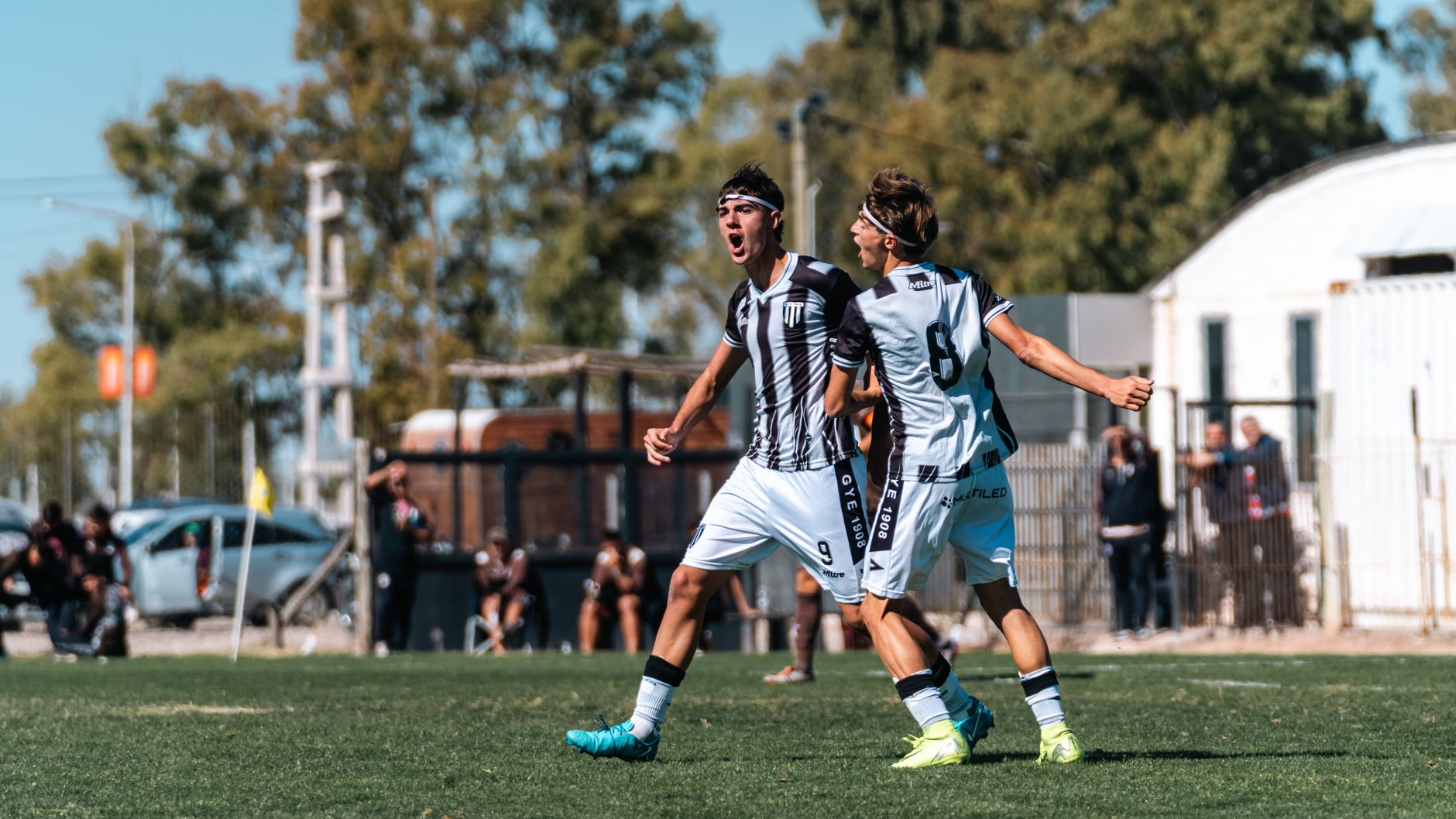 Two soccer players in action celebrating a goal on the field under clear skies.