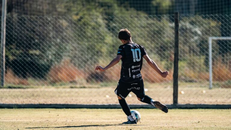 Young soccer player in black jersey with number 10 kicking a ball during a game on a sunny outdoor field.