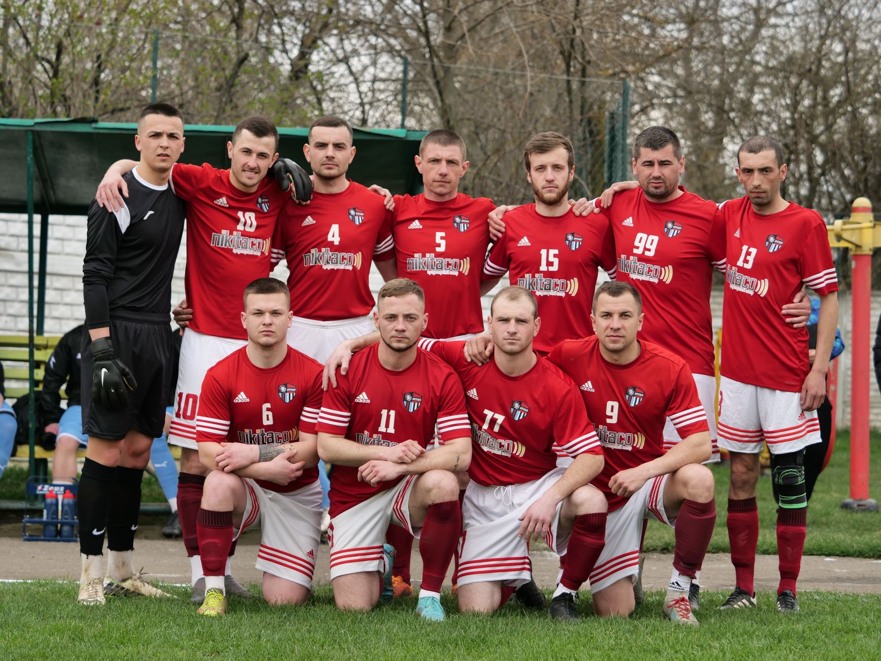 A group of football players in red uniforms posing together on the field.