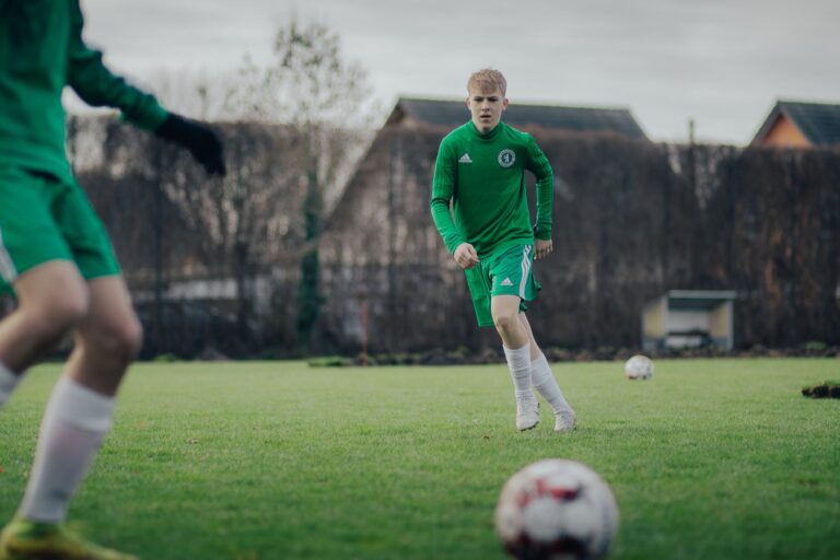 Two teenagers playing soccer on a grass pitch during daytime training session.