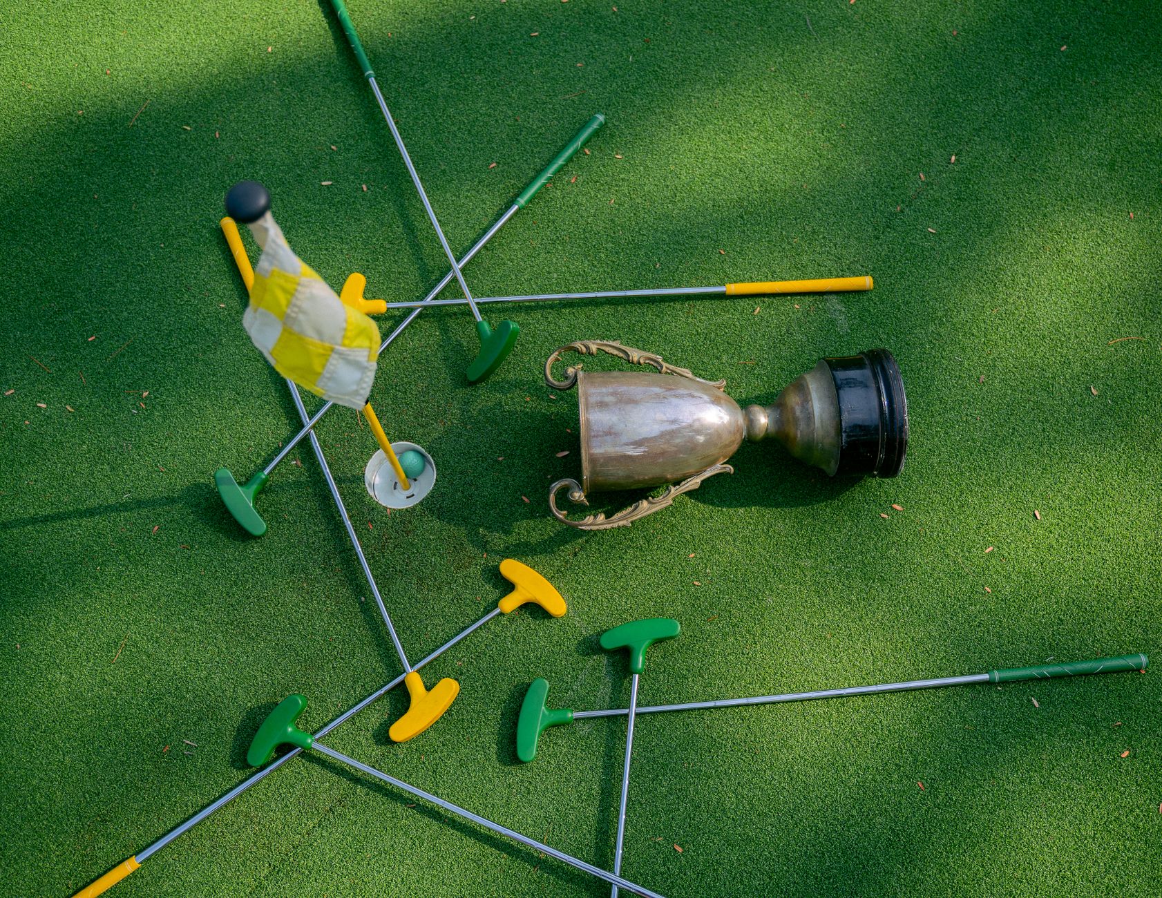 Mini golf setup with colorful putters, a cup, and a flag on green turf. Ideal for casual sports and recreation themes.