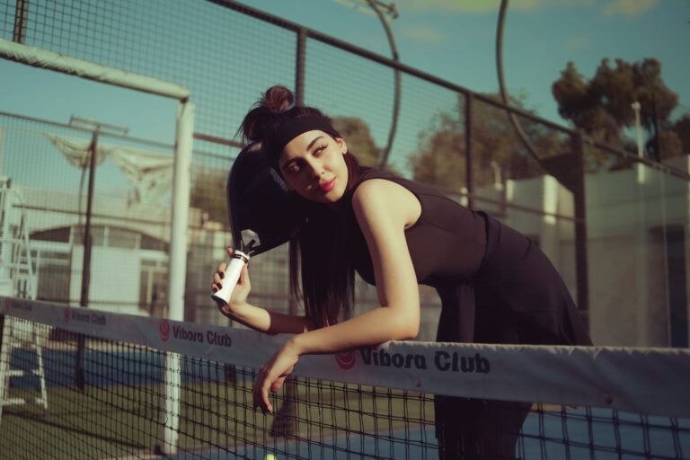A young woman leaning on a tennis net outdoors on a sunny day in Baghdad, Iraq.