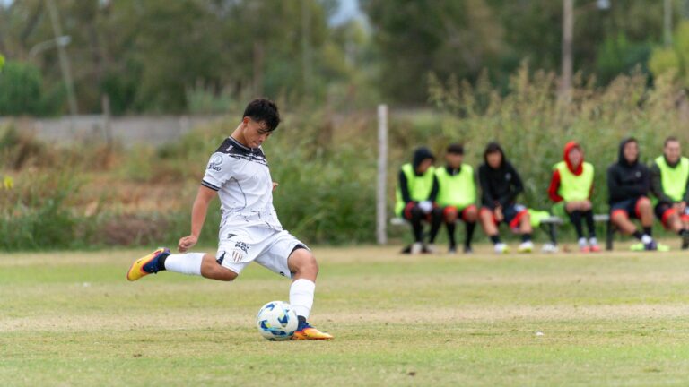 A soccer player is captured in action, kicking a ball mid-game outdoors on a grass field.