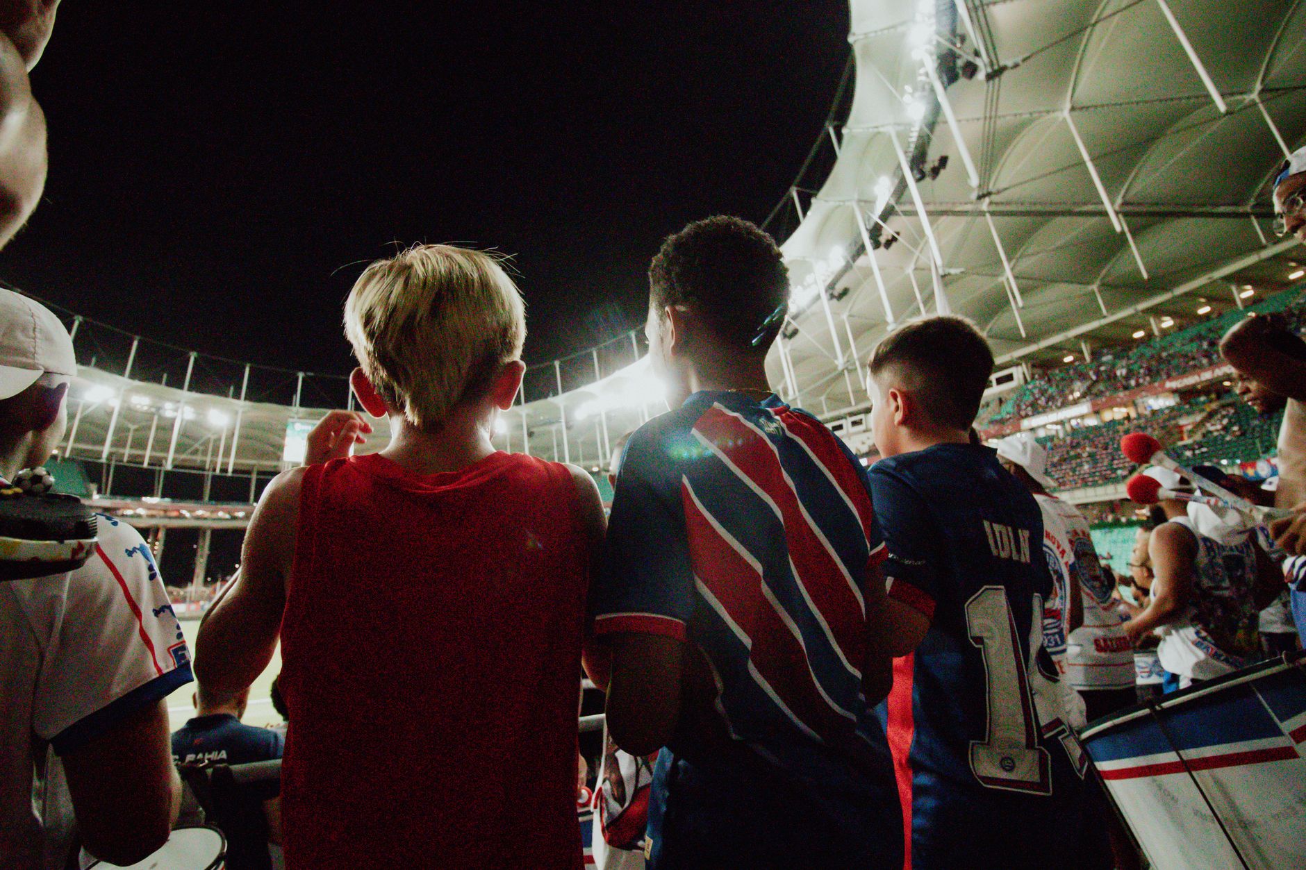 Fans cheer from the stands during a night soccer game in a large stadium, full of energy and excitement.