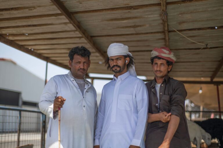 Three shepherds standing in a barn wearing traditional attire, showcasing rural life.
