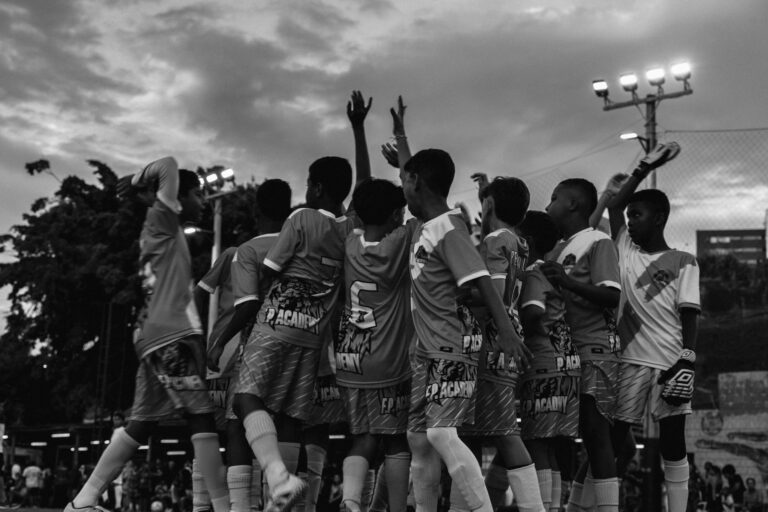 A group of young boys celebrating their soccer victory outdoors at dusk.
