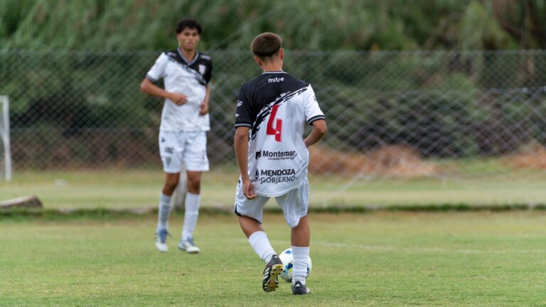Two youths playing soccer on a grassy field, wearing team jerseys.