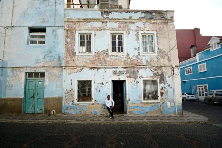 A weathered building with a man sitting outside in the urban streets of Mindelo, Cape Verde.