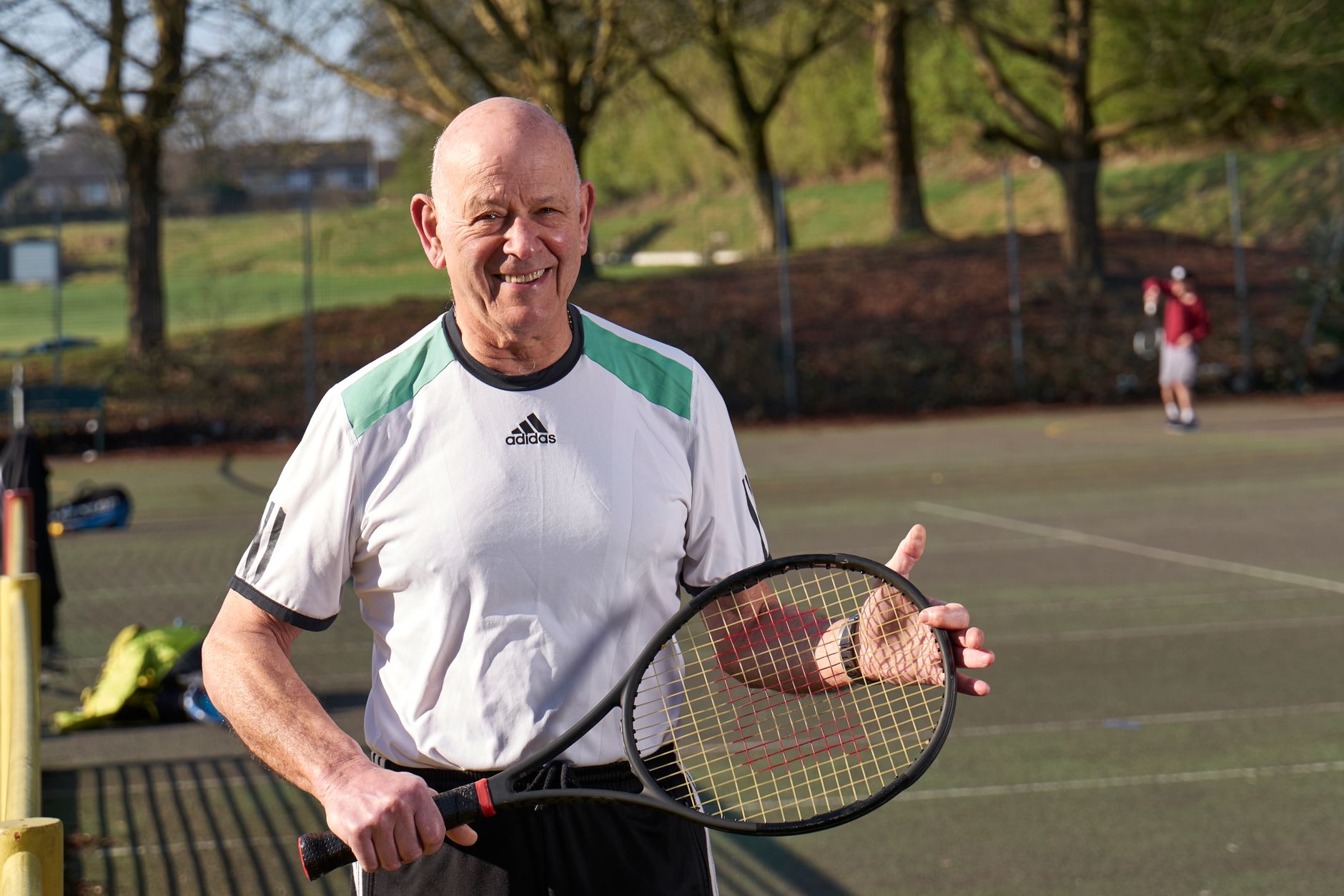 Senior adult man enjoying a sunny day playing tennis on an outdoor court.