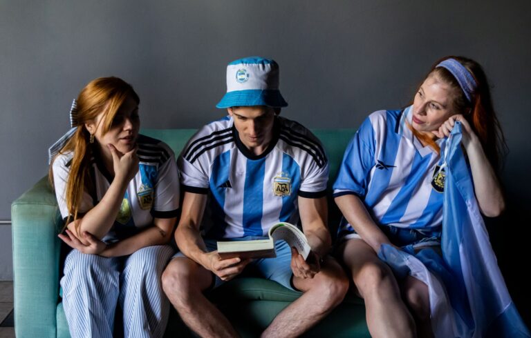 Three people wearing Argentina jerseys sitting on a couch, enjoying leisure time.