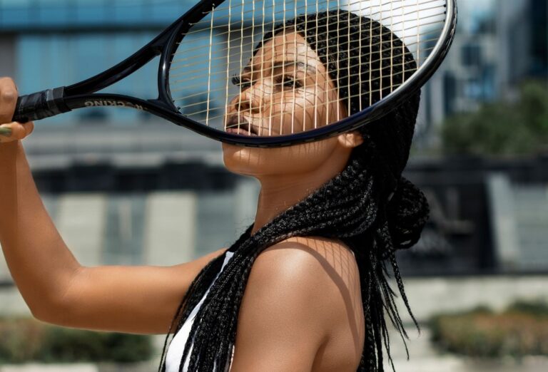 Fashionable young woman with braided hair posing with a tennis racket in an urban setting.