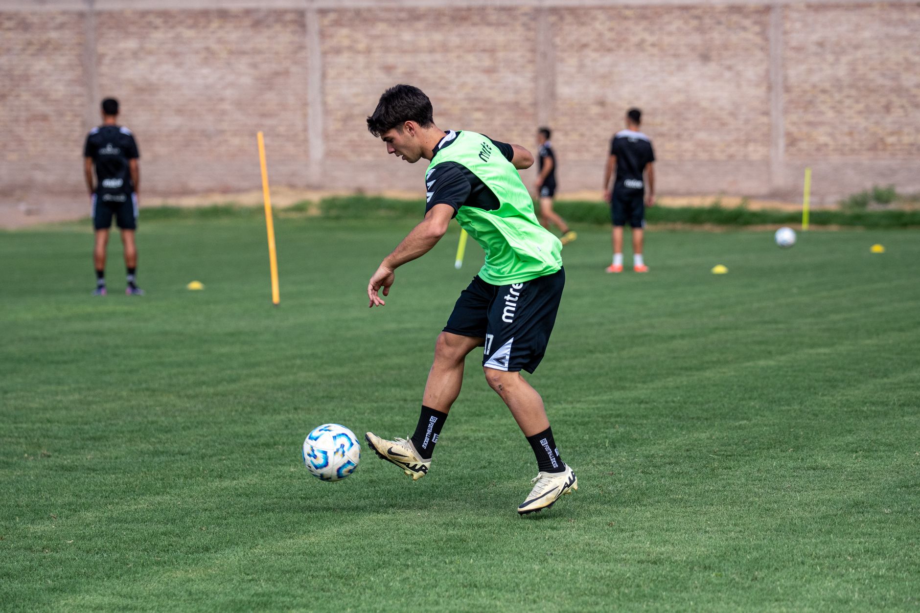 A young male soccer player performing dribbling drills on an outdoor field during daytime practice.