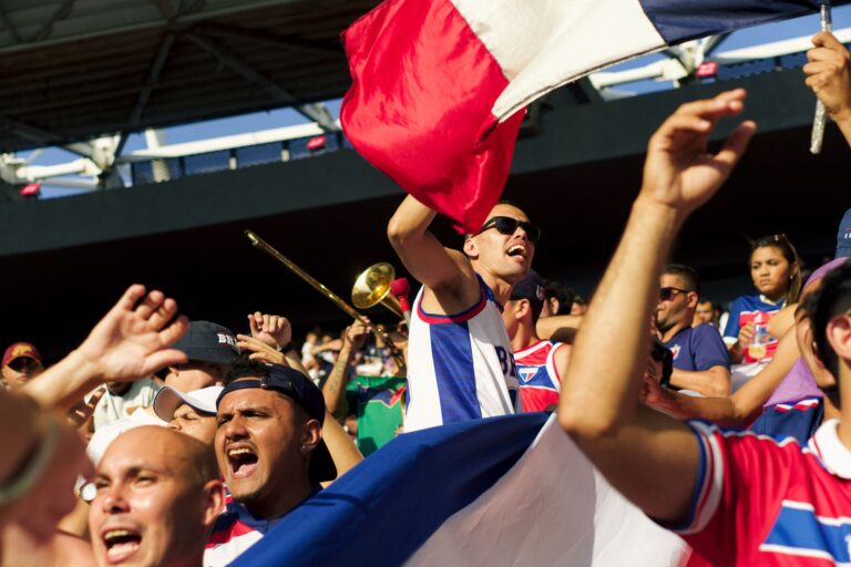 A lively group of soccer fans celebrating energetically with flags and cheering in a stadium.