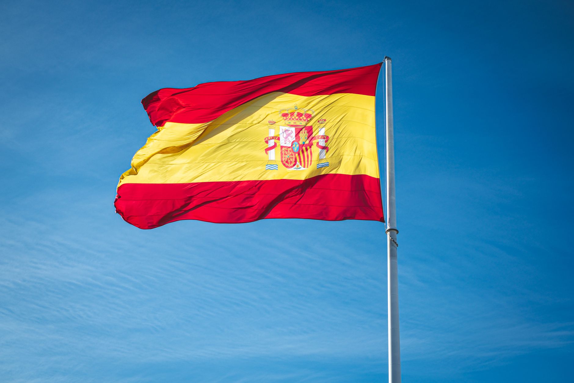 Vibrant Spanish flag waving proudly against a clear blue sky, symbolizing national pride.