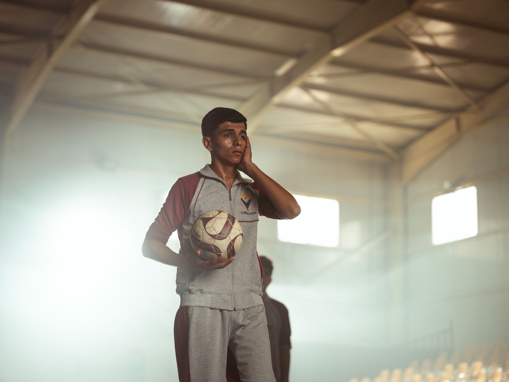Teenager in sports gear holding a soccer ball inside an indoor arena in Baghdad, Iraq.