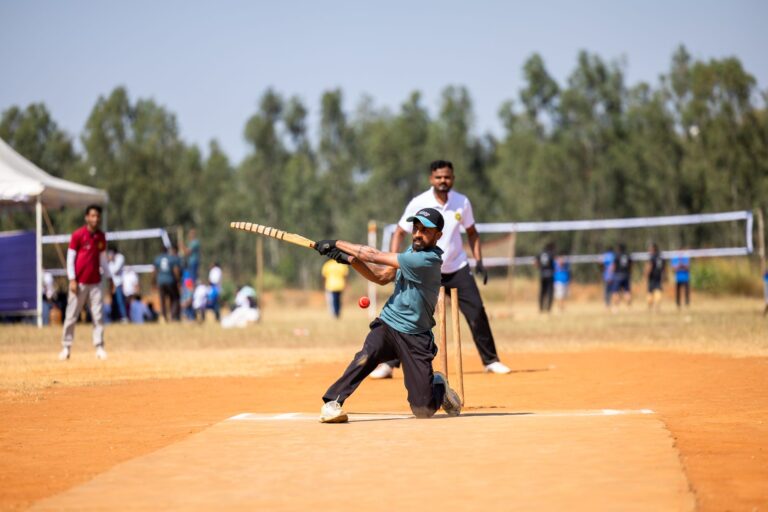 Cricket player skillfully hitting a ball during a lively outdoor match on a sunny day.