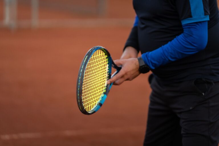 Close-up of a tennis player holding a racket on a clay court during daytime, showcasing athletic attire.