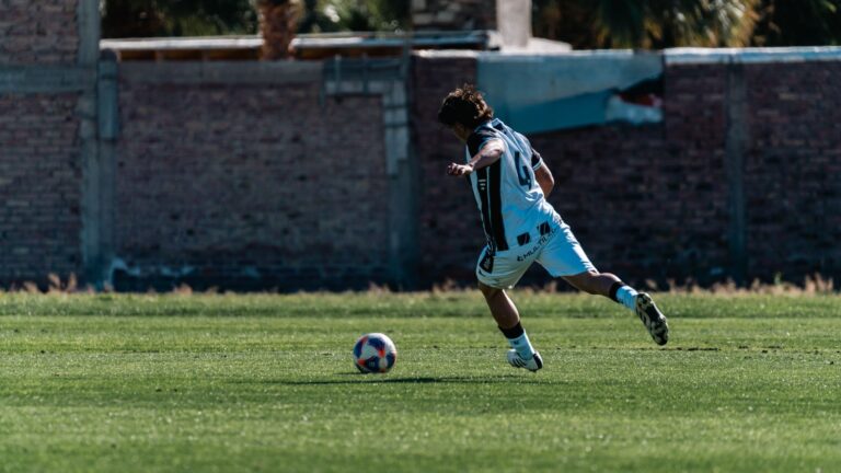 A soccer player in action kicking a ball on a grassy field outdoors.