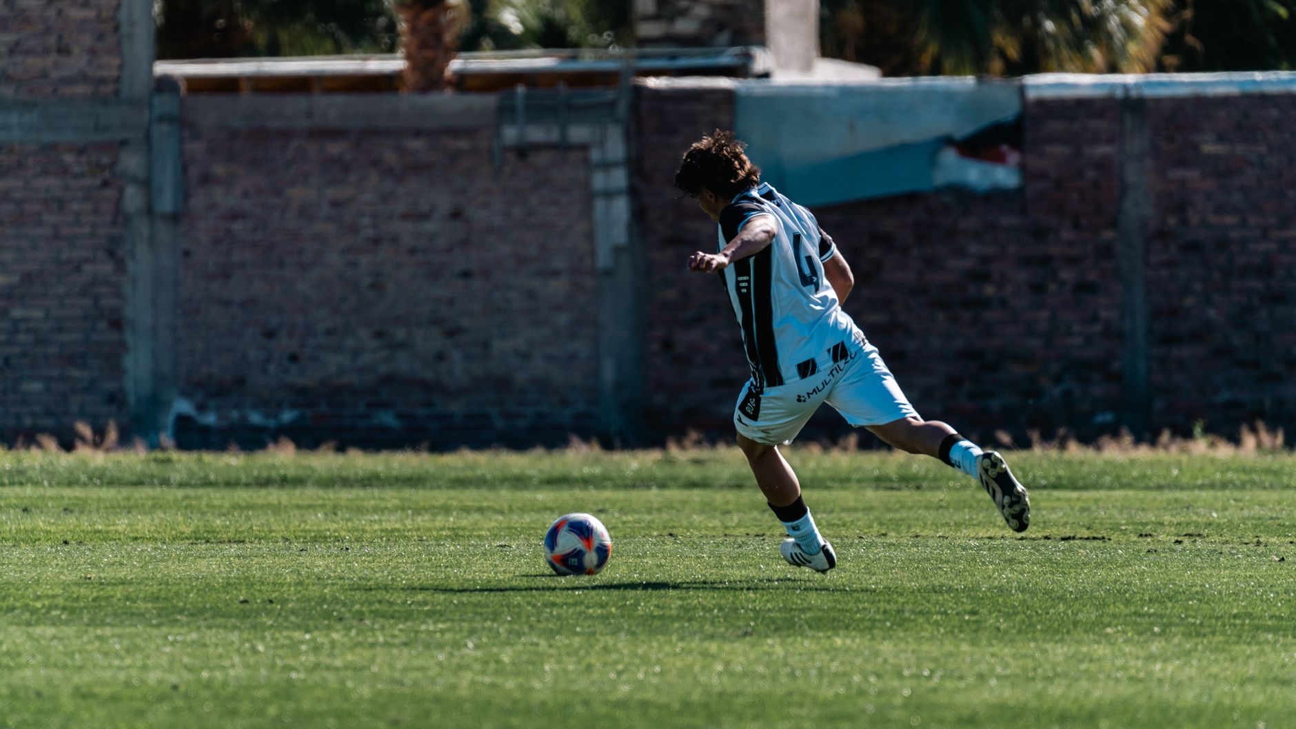 A soccer player in action kicking a ball on a grassy field outdoors.