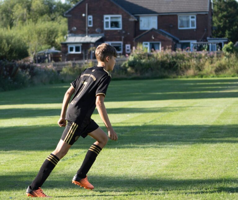 A teenager in sportswear playing soccer on a sunny day near a rural home.