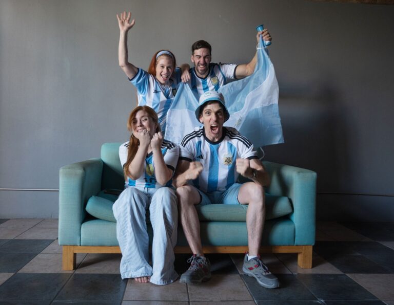 Group of enthusiastic fans in Argentina jerseys watching a soccer match indoors.