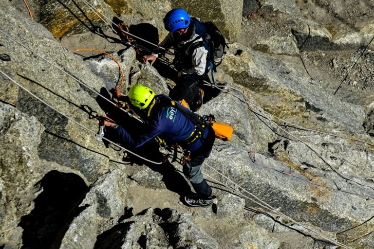Two climbers scale a rocky mountain with ropes and safety gear, showcasing adventure and teamwork.