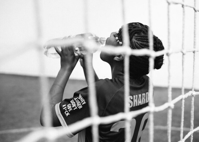 Black and white back view of young female goalkeeper drinking water from plastic bottle