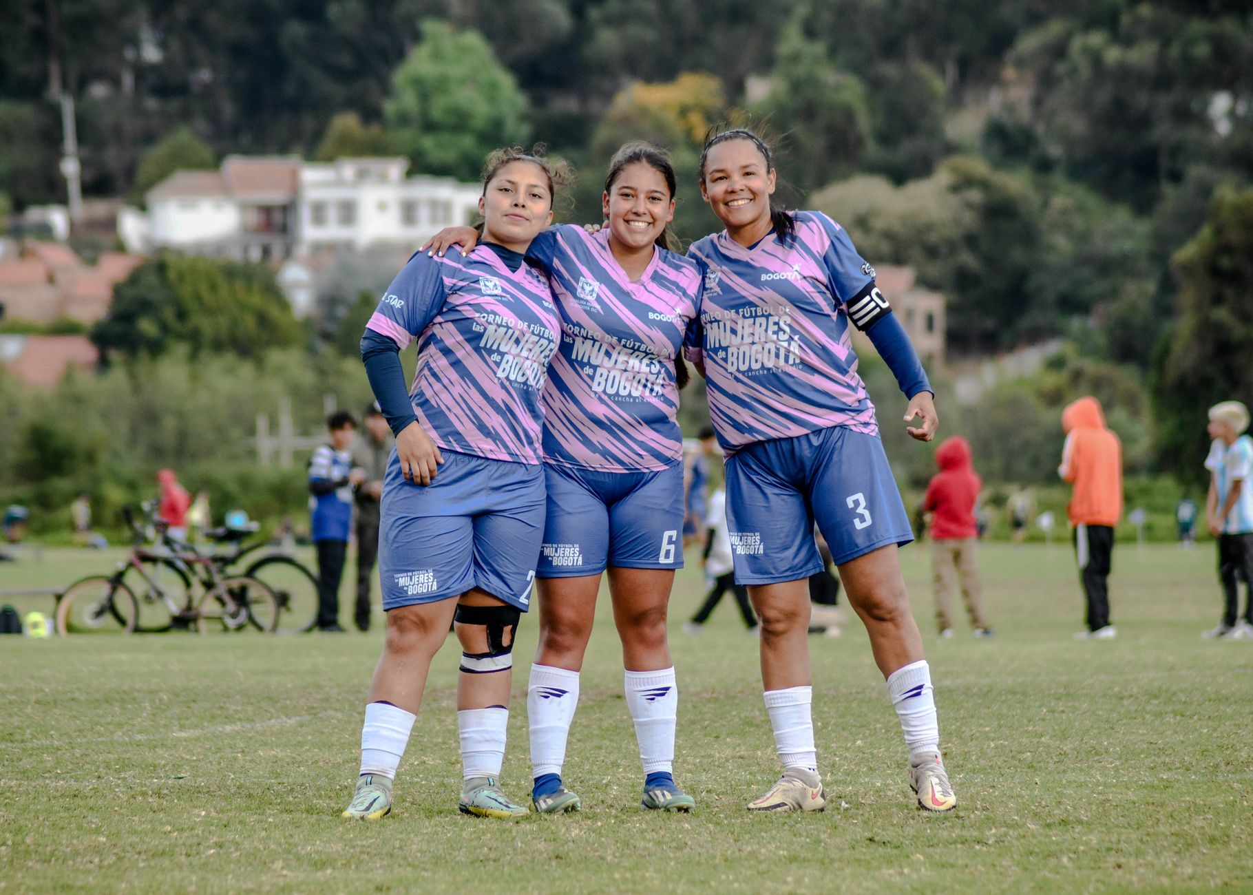 Three female soccer players in team uniform pose happily on a grass field.