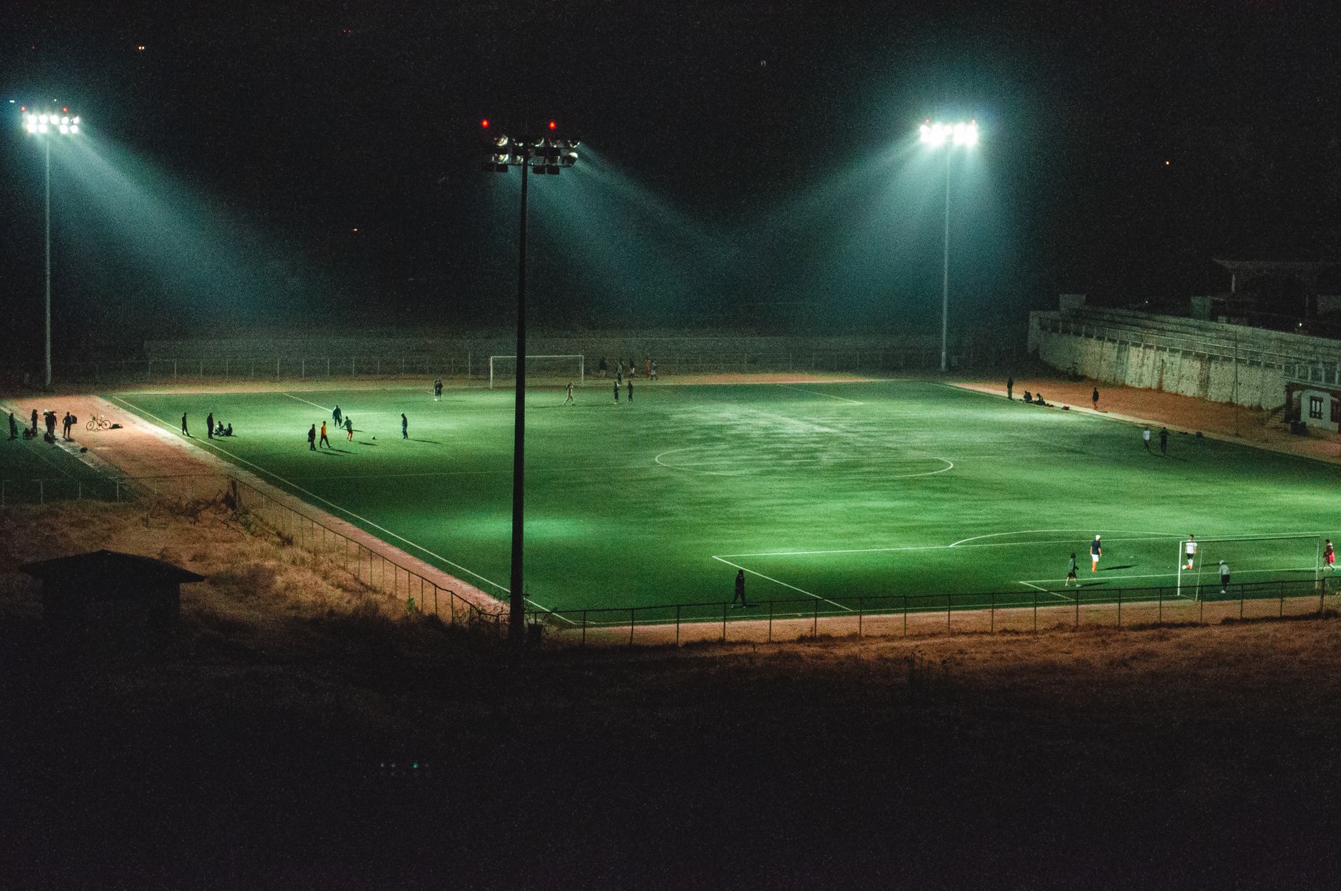 A vibrant nighttime soccer match in an illuminated stadium in Paro, Bhutan, captured from an elevated angle.