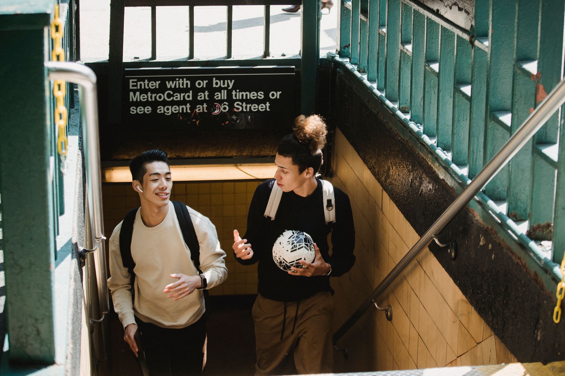 From above of friends with backpacks and ball talking to each other while exiting subway station