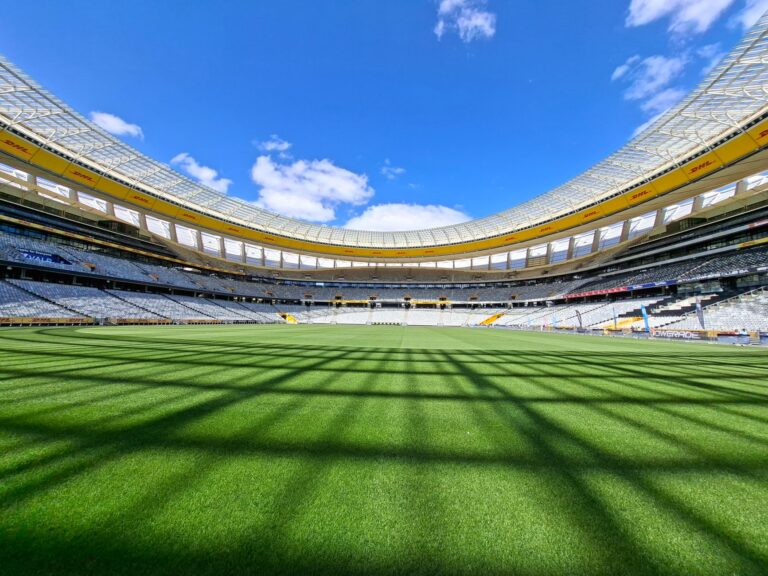 Wide-angle view of an empty stadium showcasing vibrant green grass under a clear blue sky.