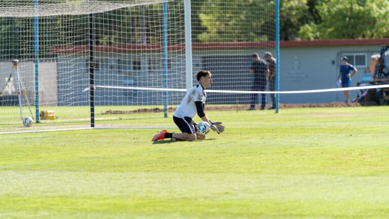 Goalkeeper kneeling with a soccer ball during outdoor training session.