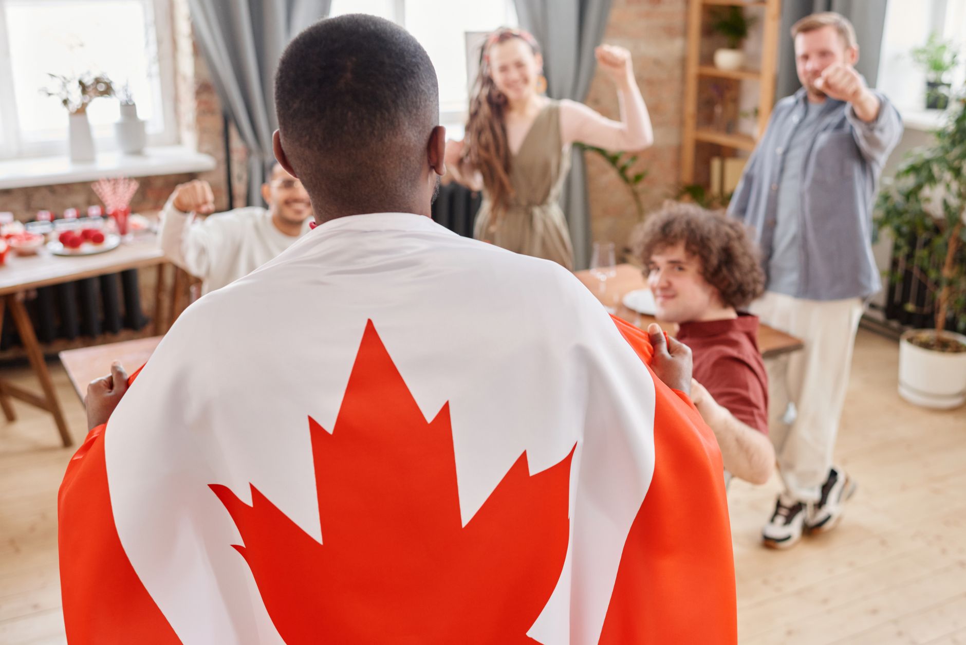 Group of friends celebrating Canada Day indoors with a Canadian flag draped over one person.