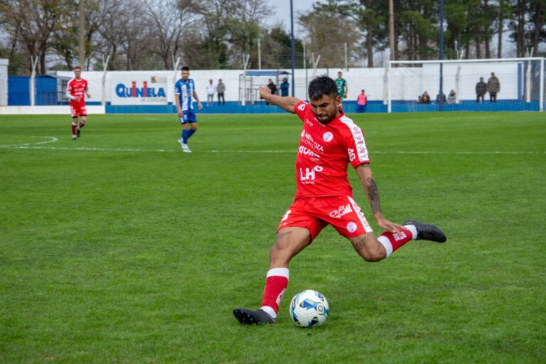 Soccer player in red jersey kicks ball during intense outdoor match.