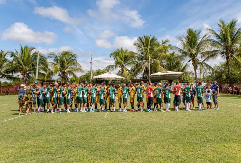 Two youth soccer teams exchange handshakes on a sunny day under palm trees.