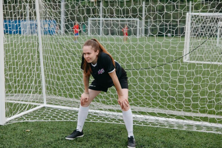 A focused female soccer player stands ready in the goal during a match on a grassy field.