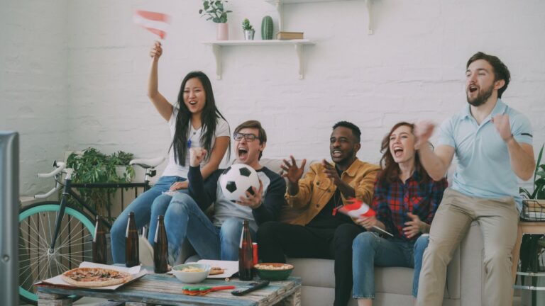 Group of friends cheering while watching a sports game on TV indoors.