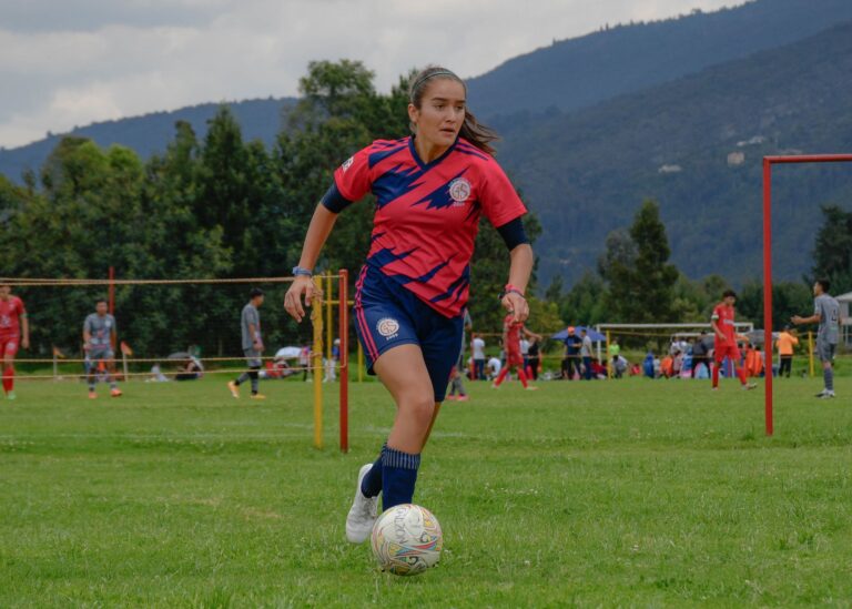 Focused young female soccer player dribbling on a lush green field during a daytime match.